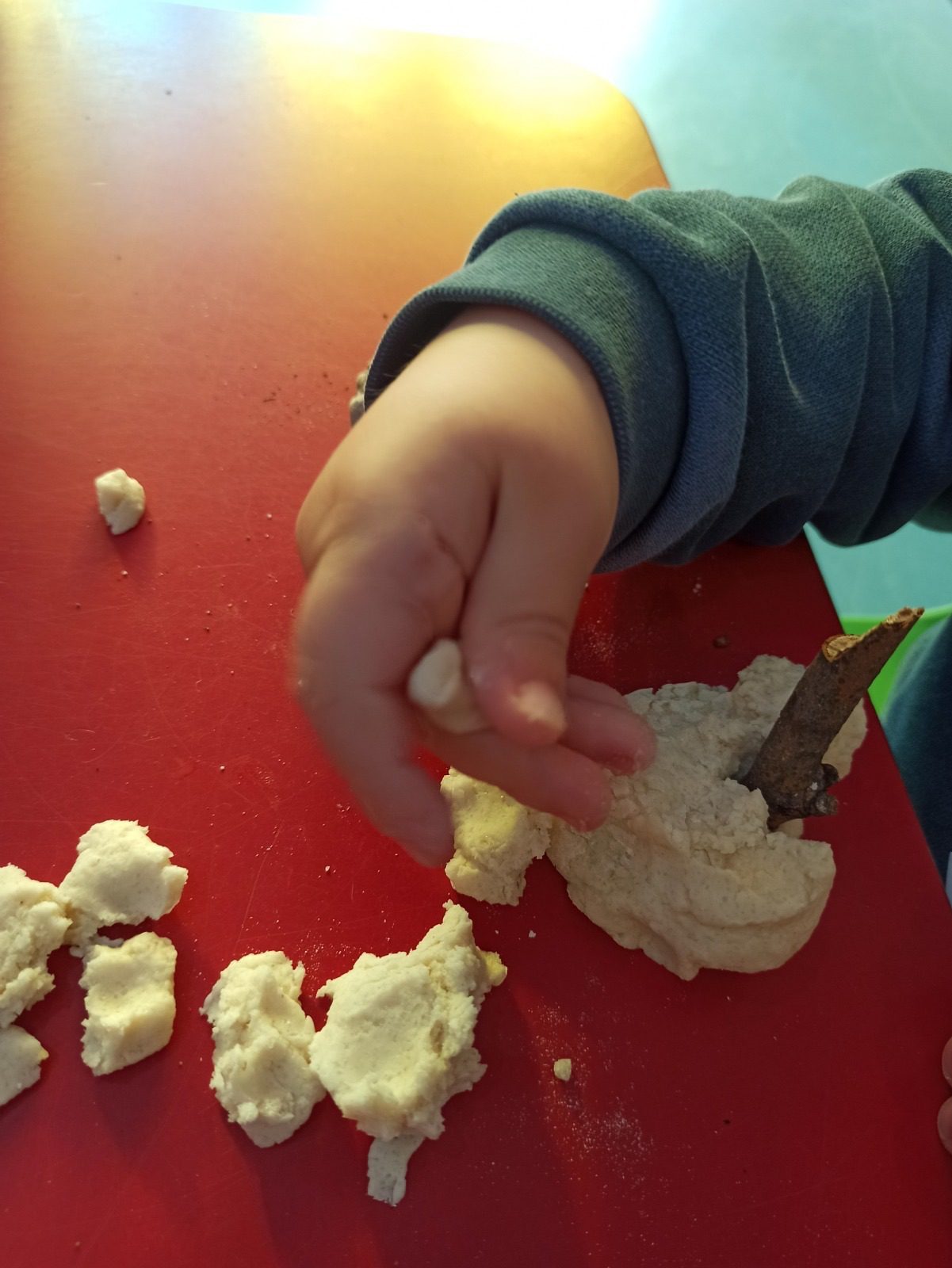 Detalle de mano infantil clavando una rama en una masa de pan blanca.