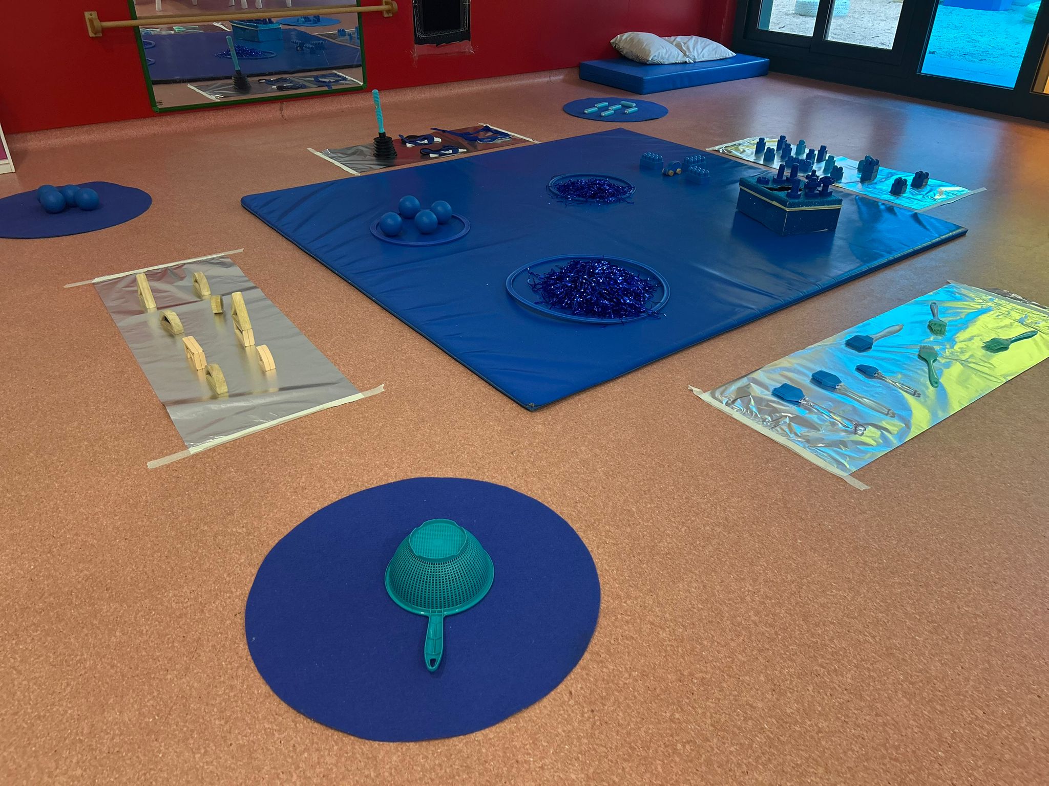 Vista panorámica de un aula infantil con alfombras y materiales de juego de color azul.