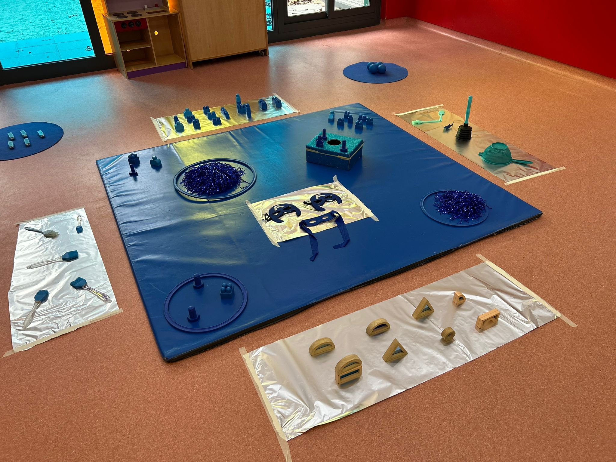 Colchoneta azul con máscaras, pompones de rafia, aros y cajas de encajar.