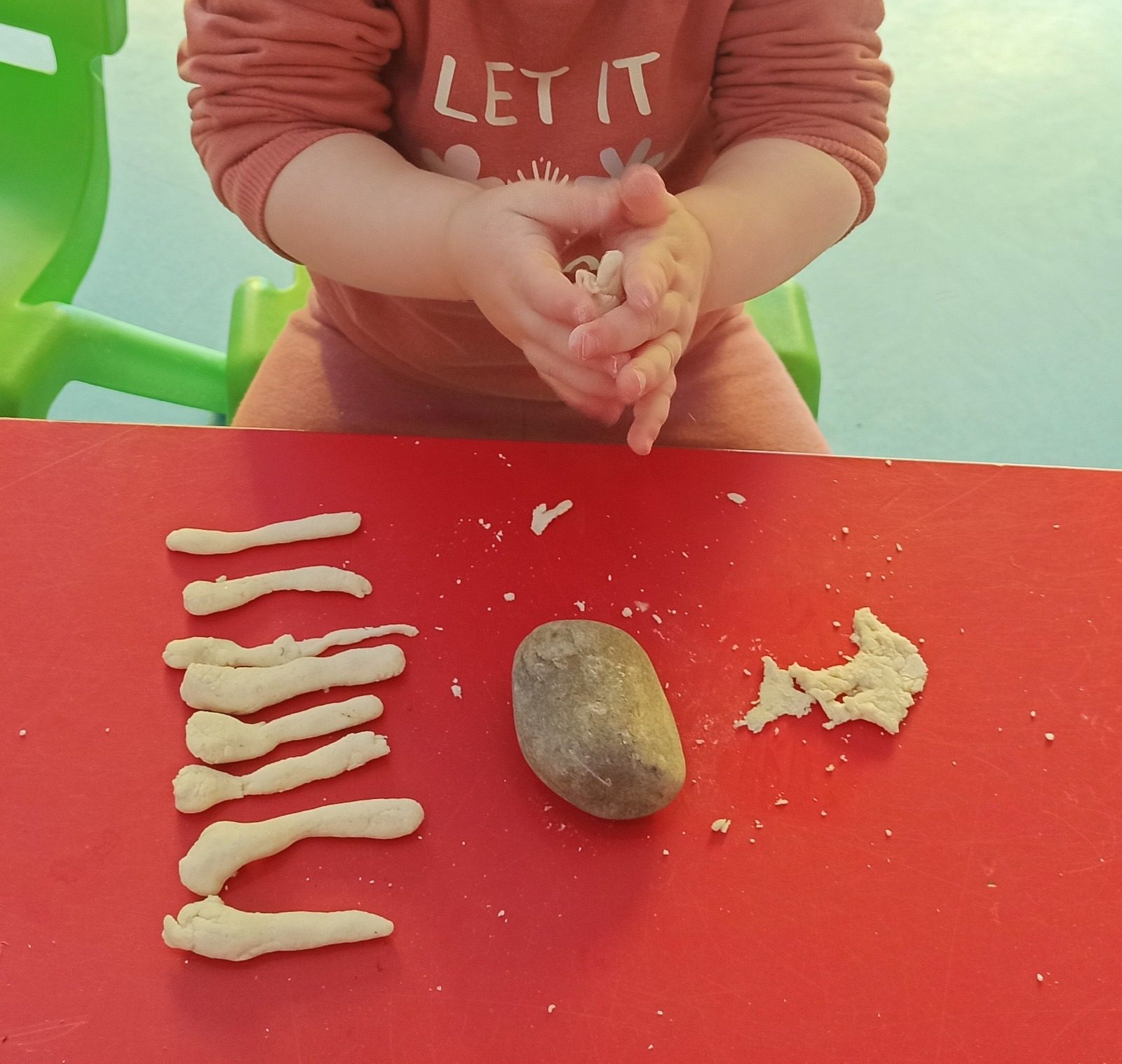 Niño pequeño moldeando tiras de masa de pan sobre una mesa roja.