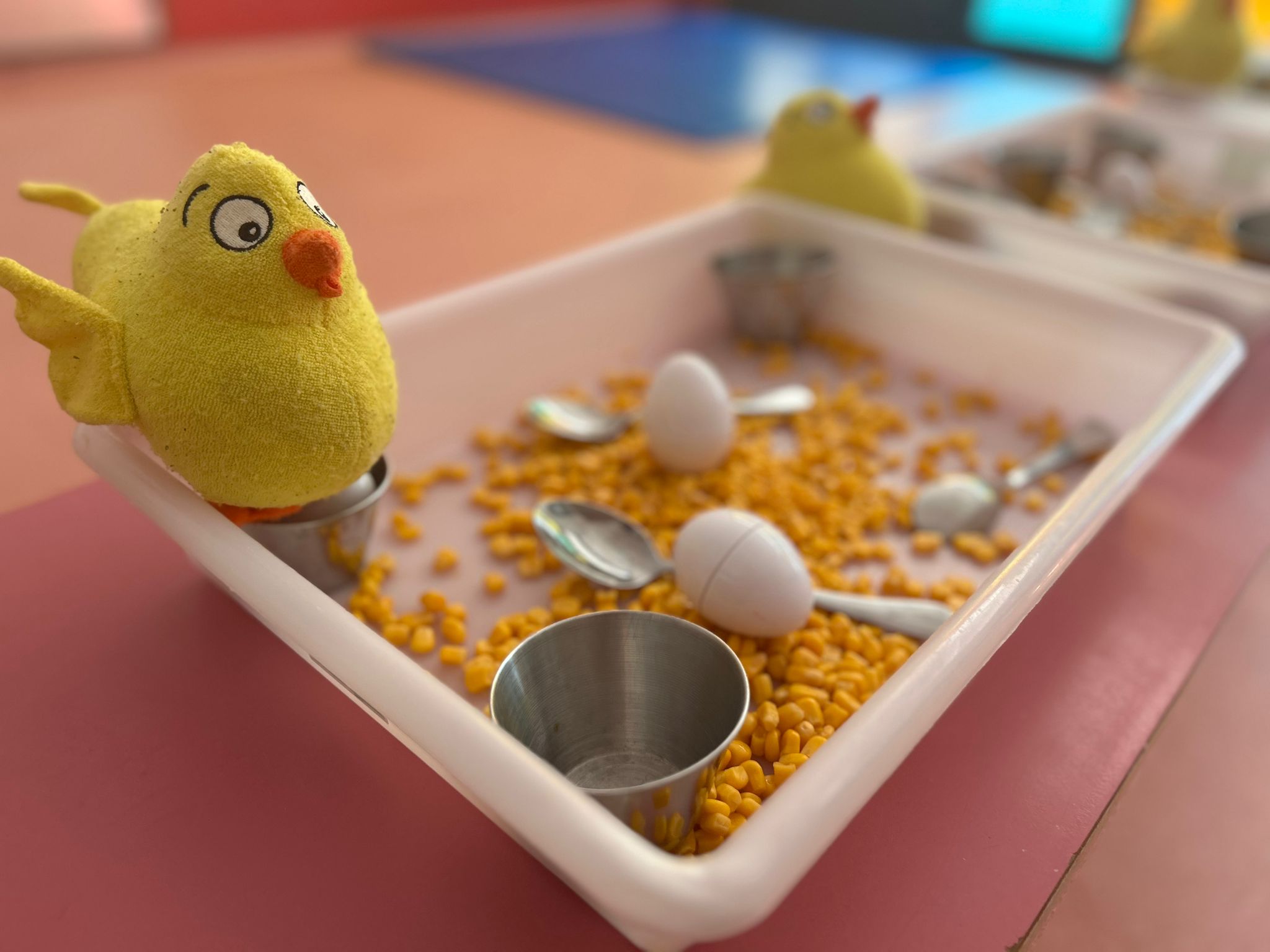 Bandeja de provocación al aprendizaje con el peluche del Pollo Pepe y granos de maíz en una guardería de Torrejón.