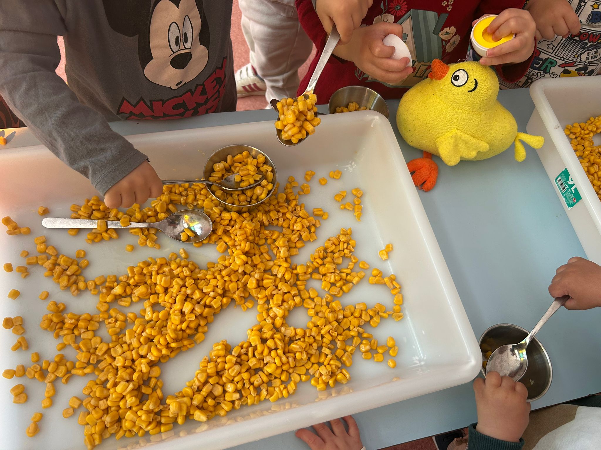 Niños de la Escuela Infantil El Gato con Botas en Torrejón de Ardoz realizando una actividad sensorial con maíz y el Pollo Pepe.