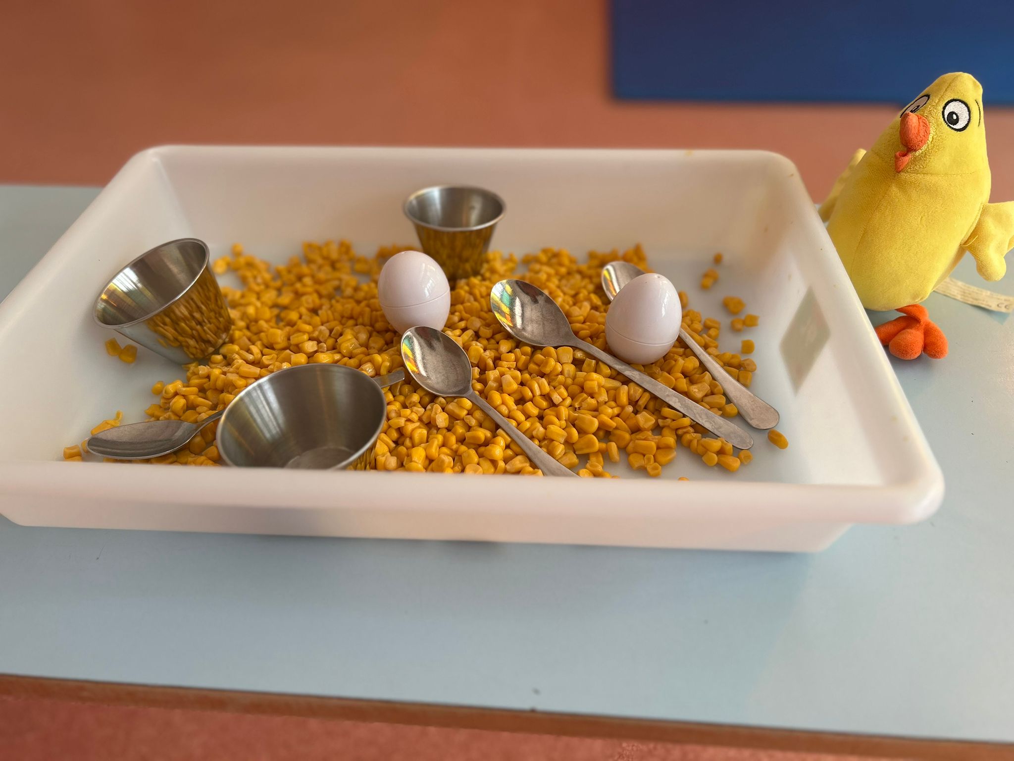 Material didáctico para estimulación sensorial: bandeja con maíz, huevos de juguete y utensilios para trasvases.