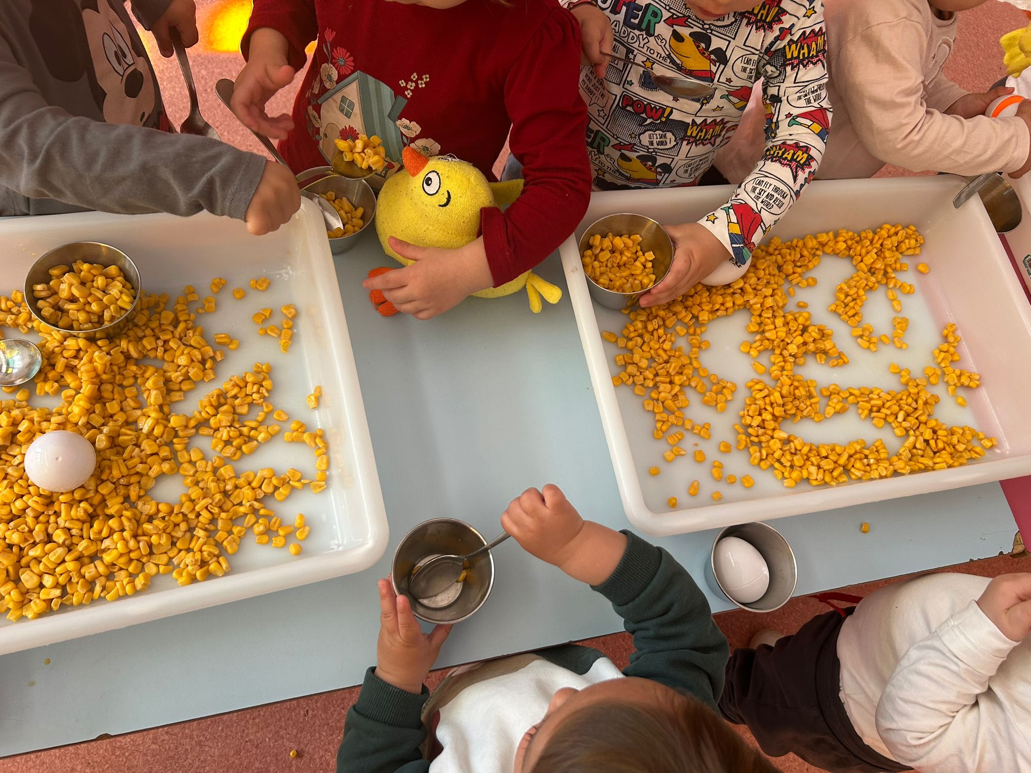 Detalle de manos de niños trabajando la psicomotricidad fina con cucharas y granos de maíz en El Gato con Botas.